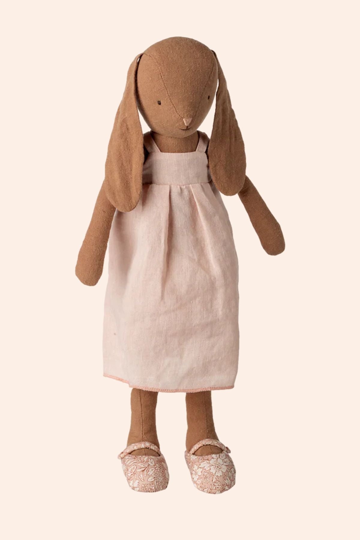Stuffed bunny doll with a pink dress on a beige background