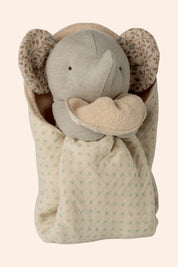 Plush elephant toy wrapped in a patterned blanket on a beige background