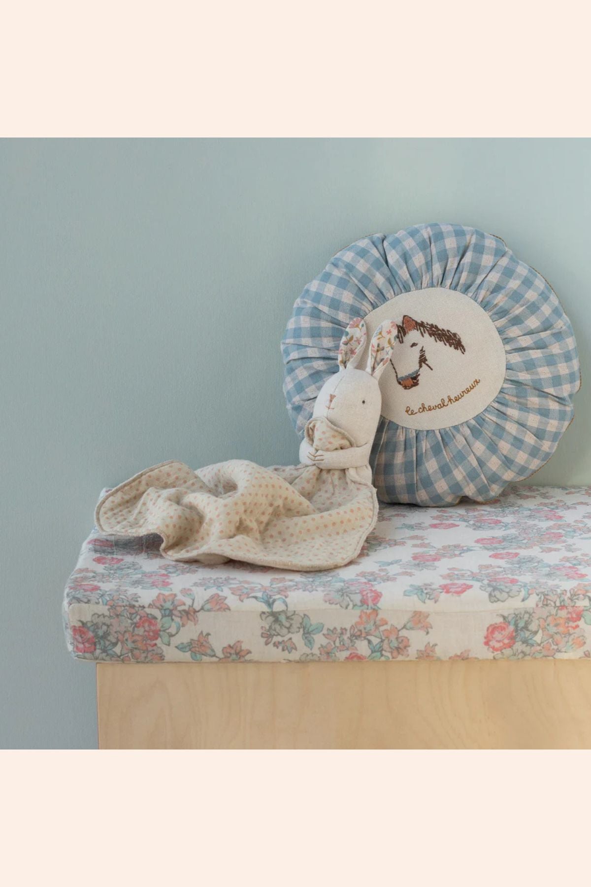 Stuffed animal toy on a floral cushion with a checkered pillow in the background